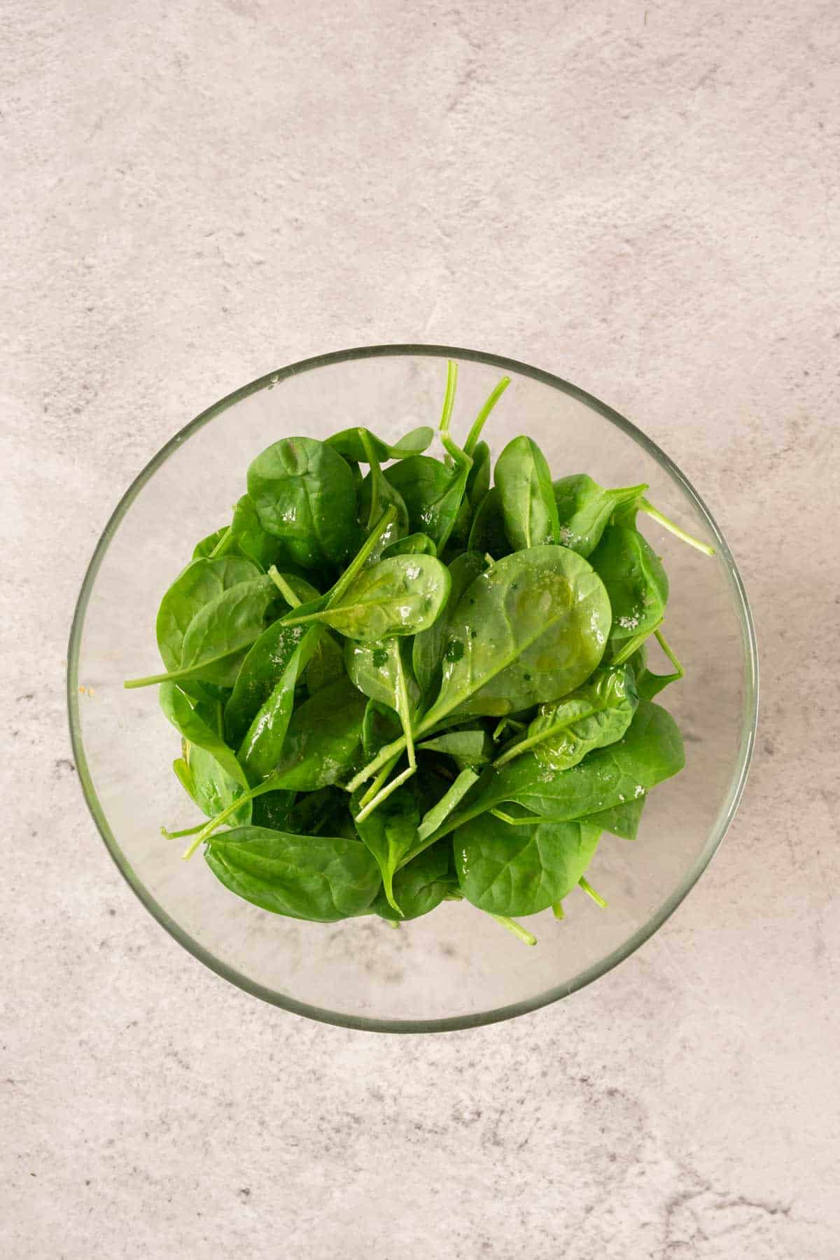 Spinach in a glass bowl on a concrete surface.