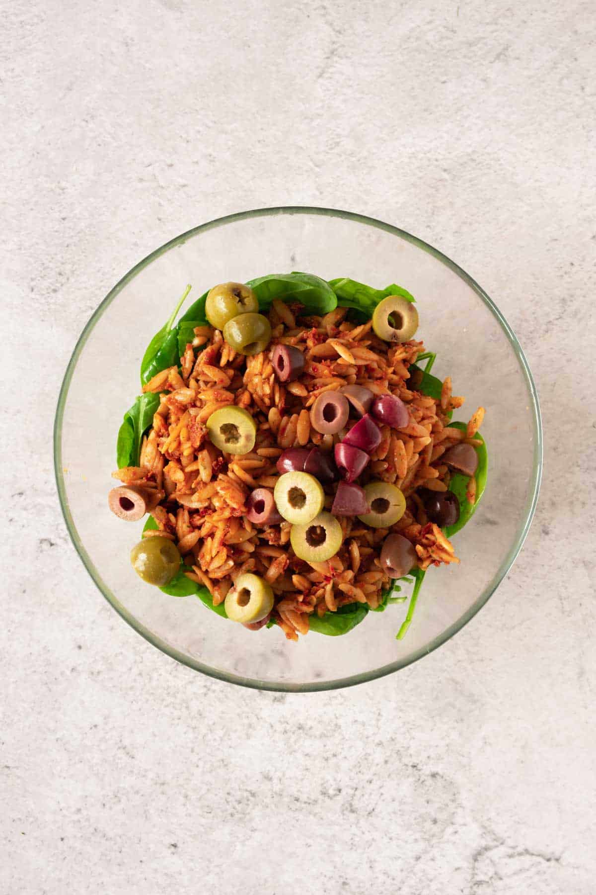 A bowl of pesto orzo pasta with olives and spinach in it.