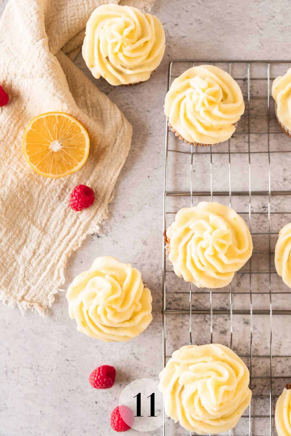 Raspberry cupcakes with lemon frosting on a cooling rack with raspberries and a lemon on the table.