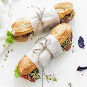 Two sandwiches wrapped in paper on a wooden table.