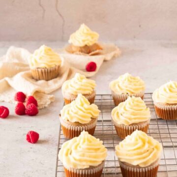 Raspberry cupcakes with lemon frosting on a cooling rack with raspberries and a lemon on the table.