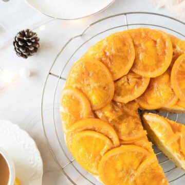 A slice of upside down orange cake on a plate with a cup of tea.