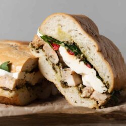 A sandwich with chicken and pesto on a wooden board.