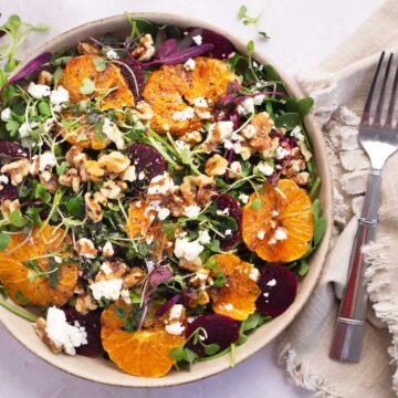 A colorful beetroot and orange salad with walnuts, cheese, and greens, served with a fork on the side.