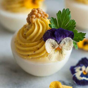 Deviled egg garnished with herbs and edible flowers on a light background.