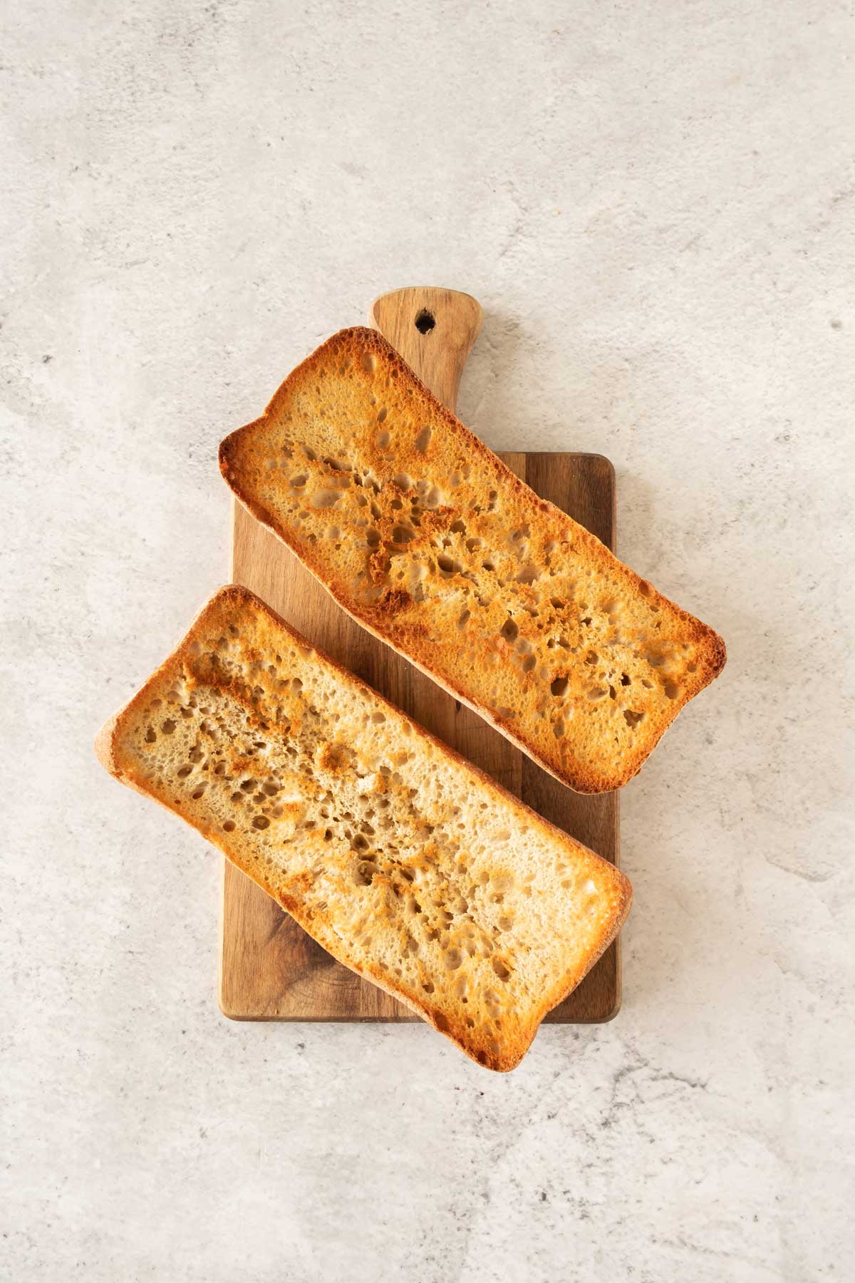Two slices of toasted bread on a wooden board with a light-colored countertop background.