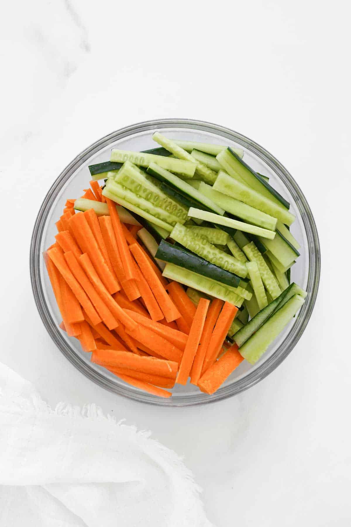 A bowl of sliced cucumbers and carrots on a white surface.