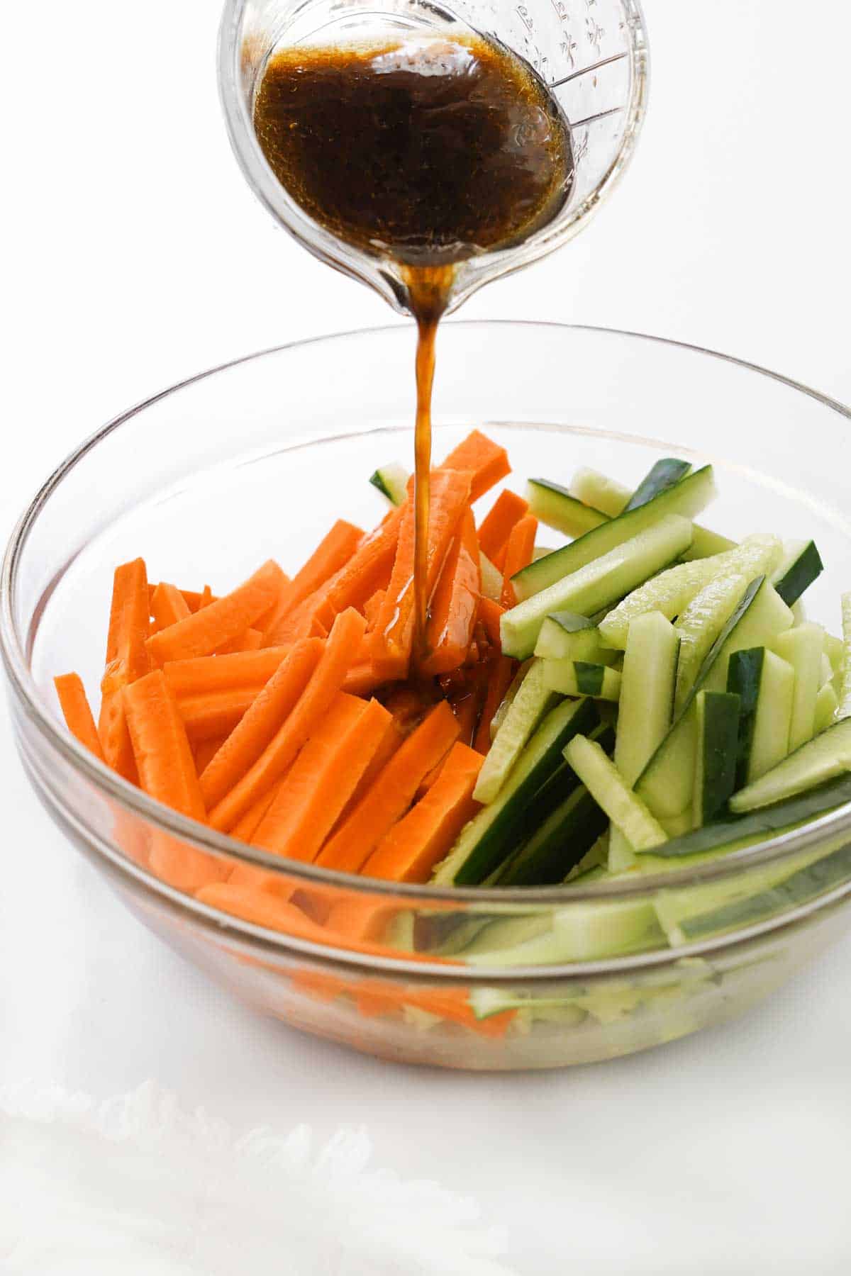 Pouring dressing over sliced carrots and cucumbers in a bowl.
