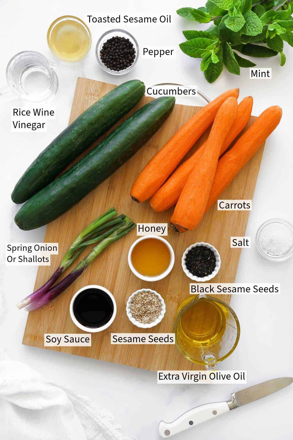 Ingredients for Carrot and Cucumber Salad recipe neatly arranged on a white surface, labeled with their names.