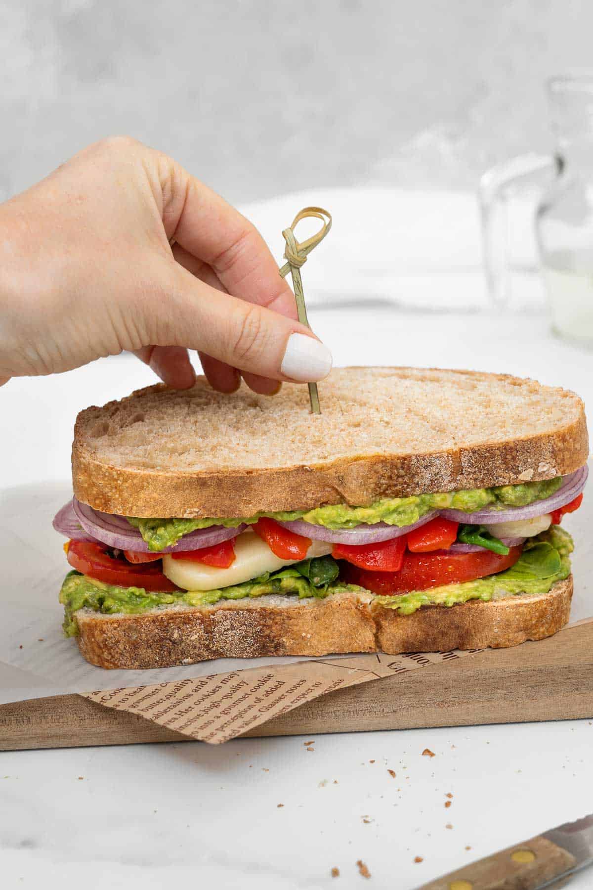 A person putting a toothpick in a vegetarian mediterranean sandwich.