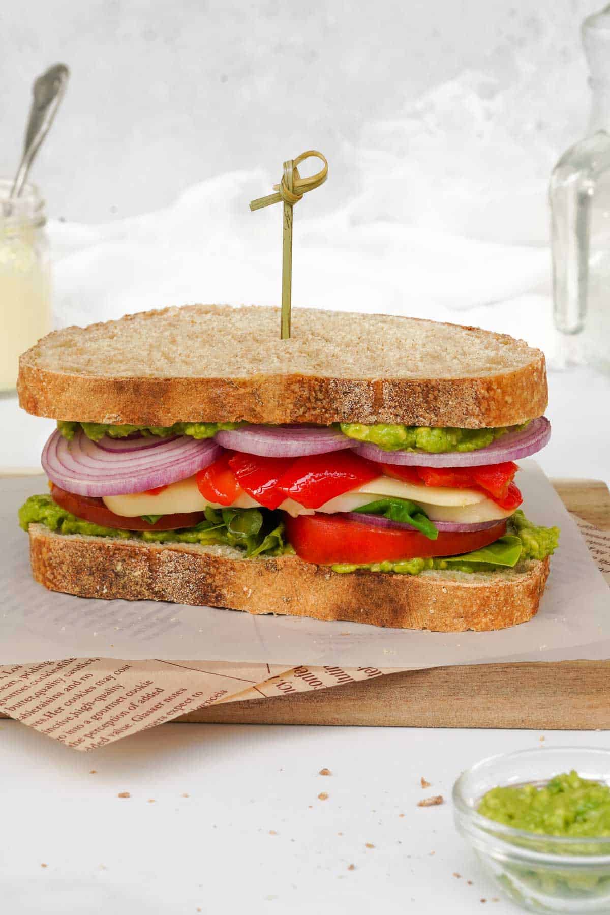 A vegetarian, Mediterranean sandwich is sitting on a cutting board next to chips.