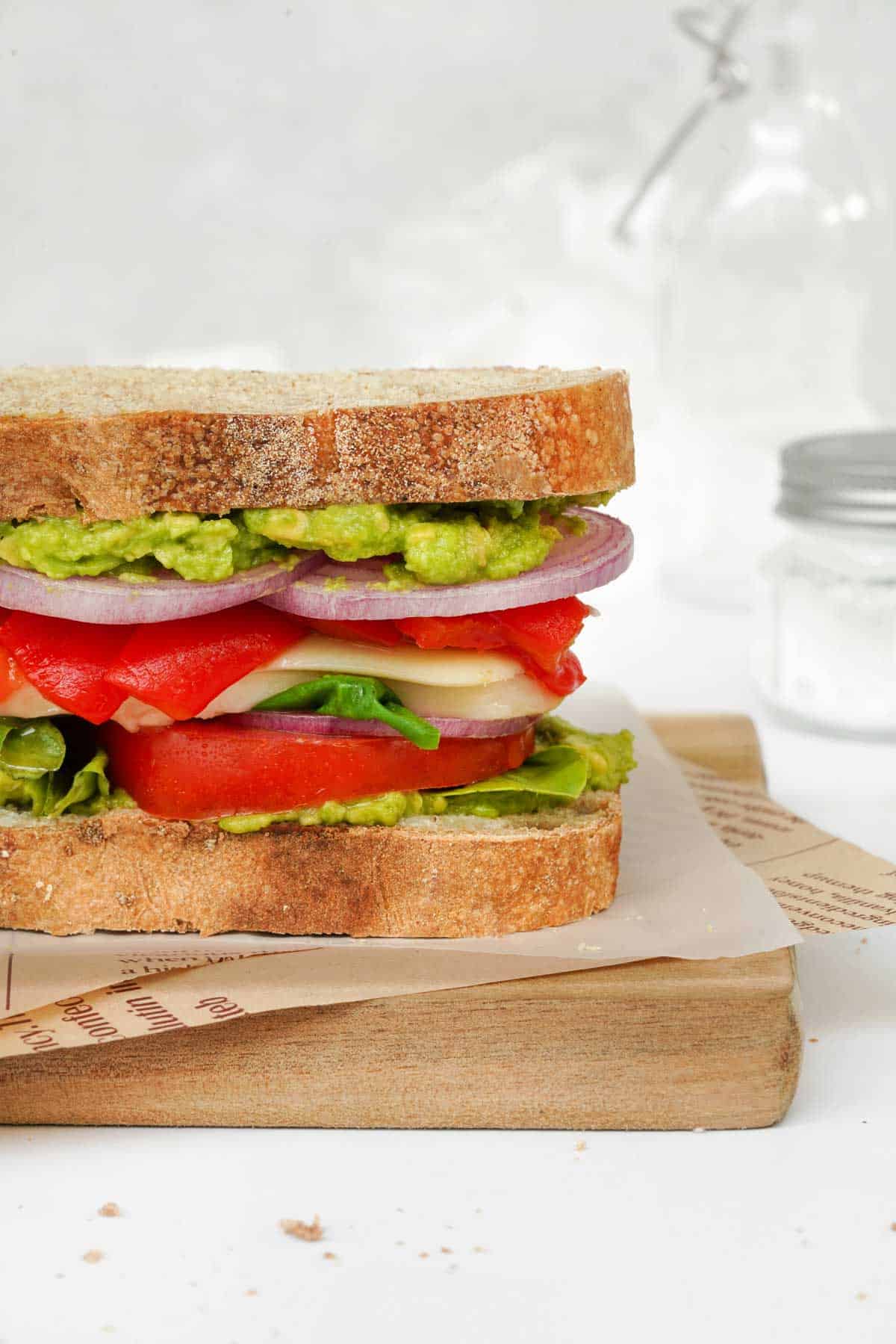 A vegetarian, Mediterranean sandwich is sitting on a cutting board.
