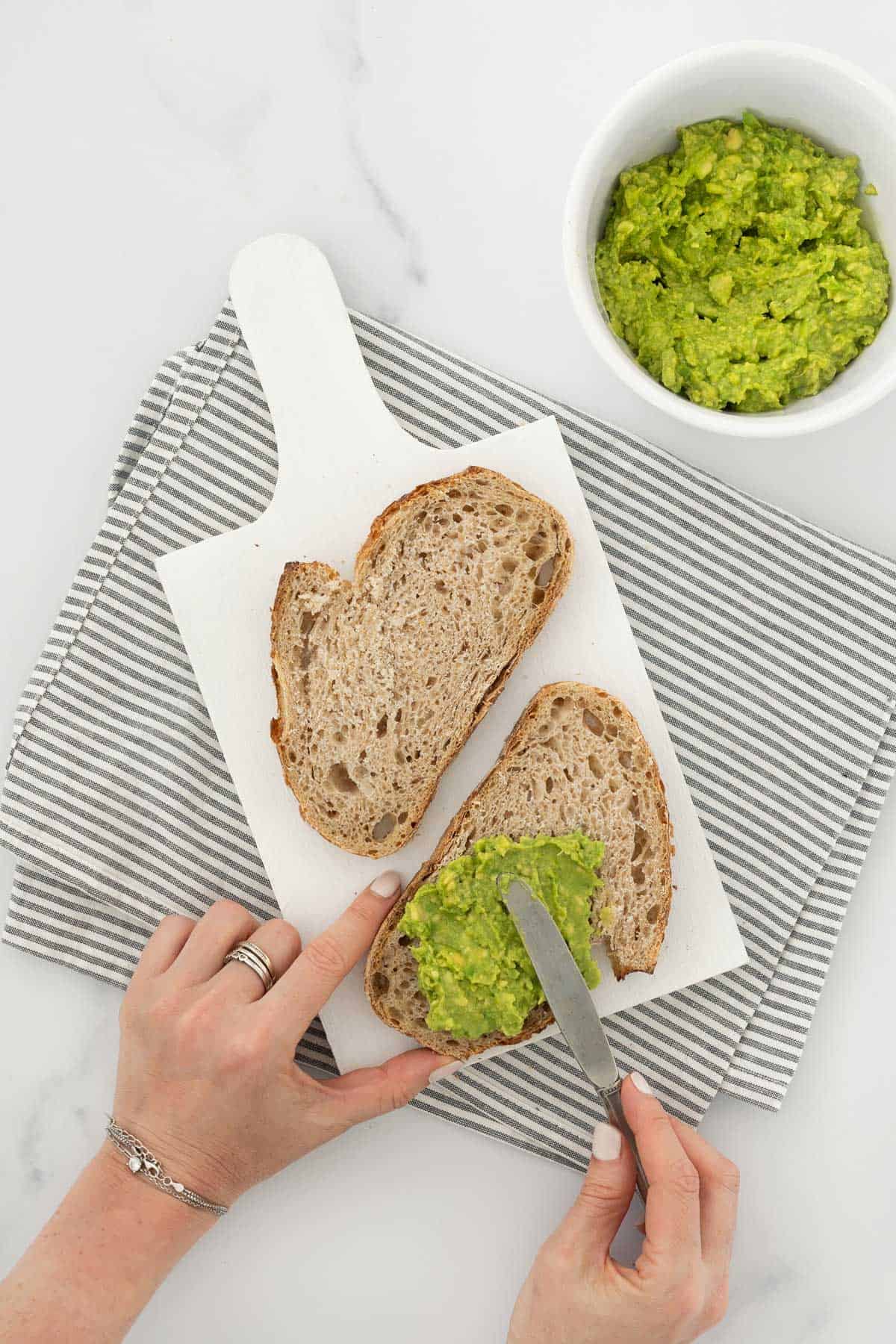 A person spreading mashed avocado on slices of bread for a sandwich.