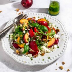 A fresh nectarine salad with spinach, nuts, and cheese, with a dressing on the side.