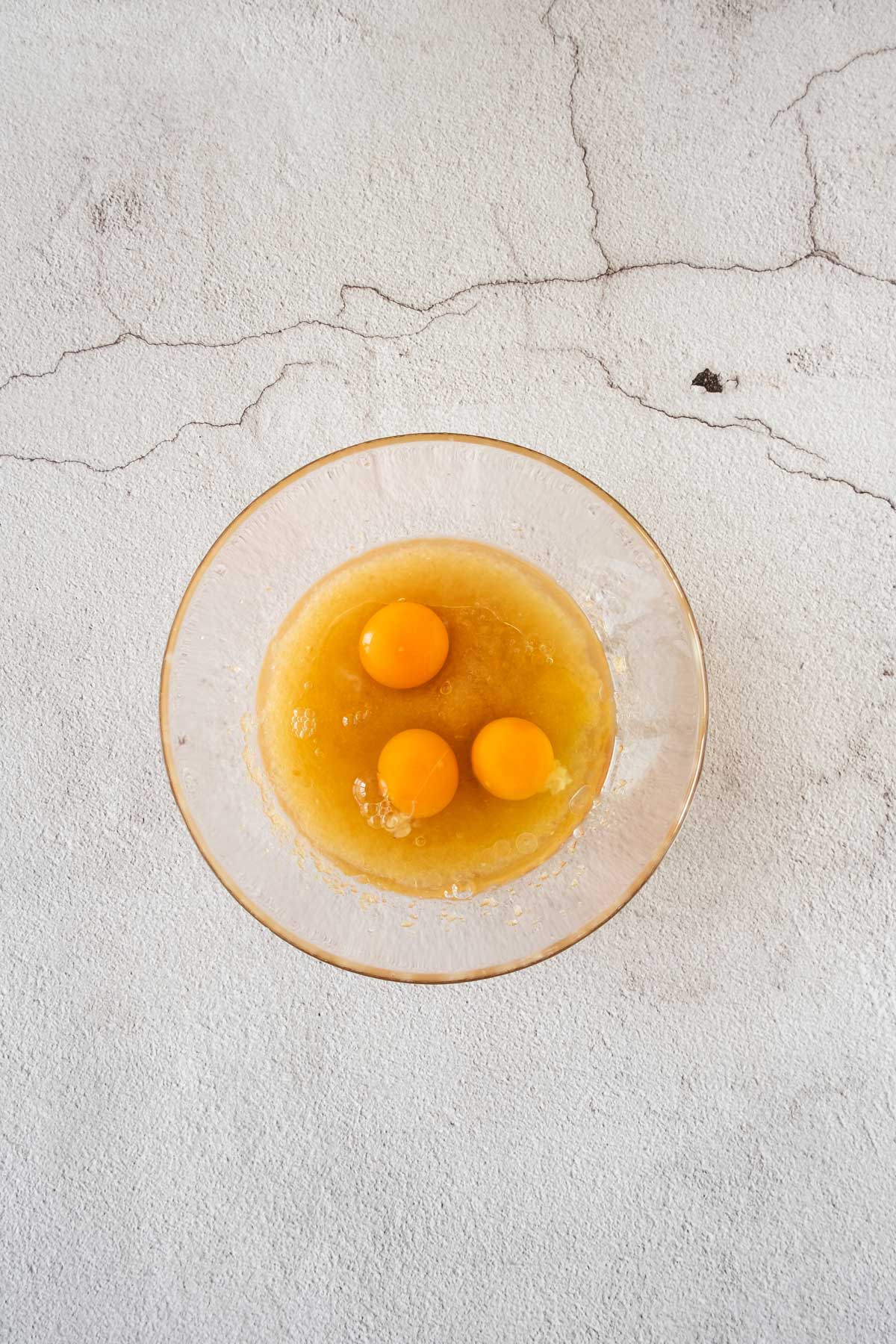 A glass bowl with oil, sugar and three eggs for a cake recipe.