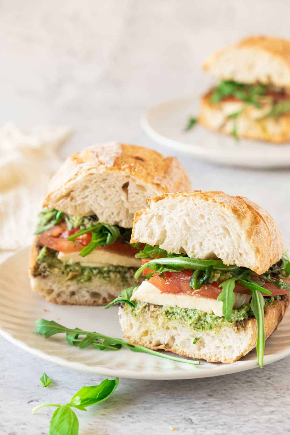 A Caprese sandwich with pesto, tomatoes and basil on a plate.