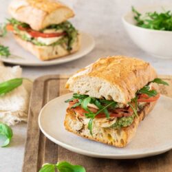 A Caprese baguette sandwich with pesto, tomatoes and basil on a plate.