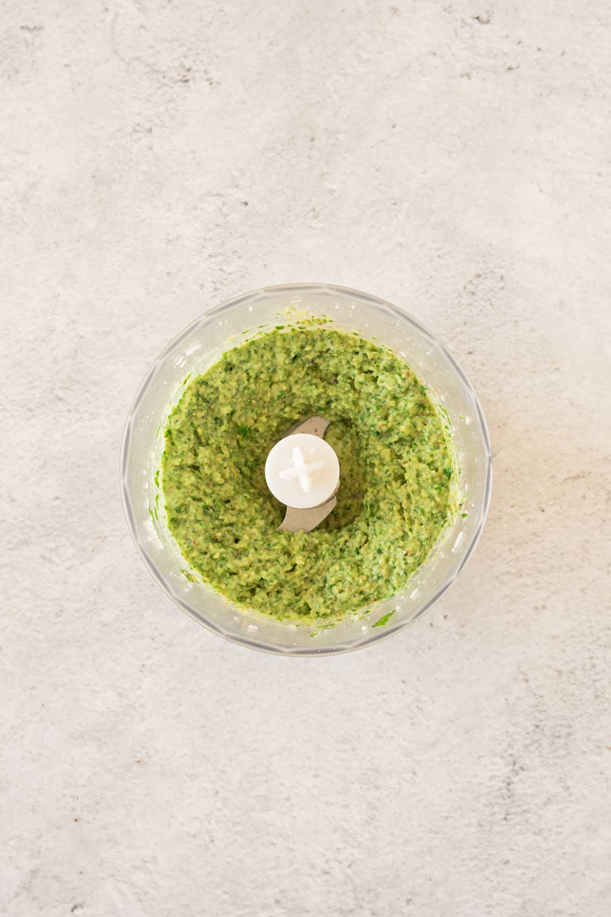 A bowl of green pesto on a white surface.