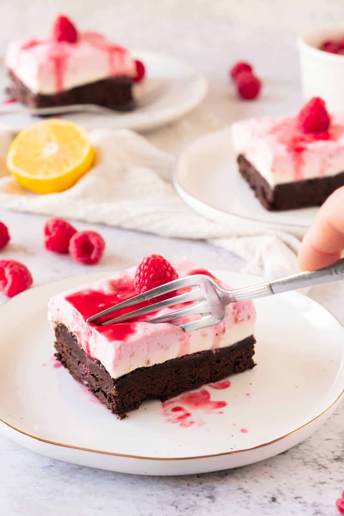 A person using a fork to take a piece from a square of Raspberry Cheesecake brownie.