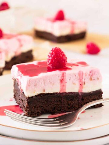 A square of Raspberry Cheesecake Brownie on a plate with a fork in front.