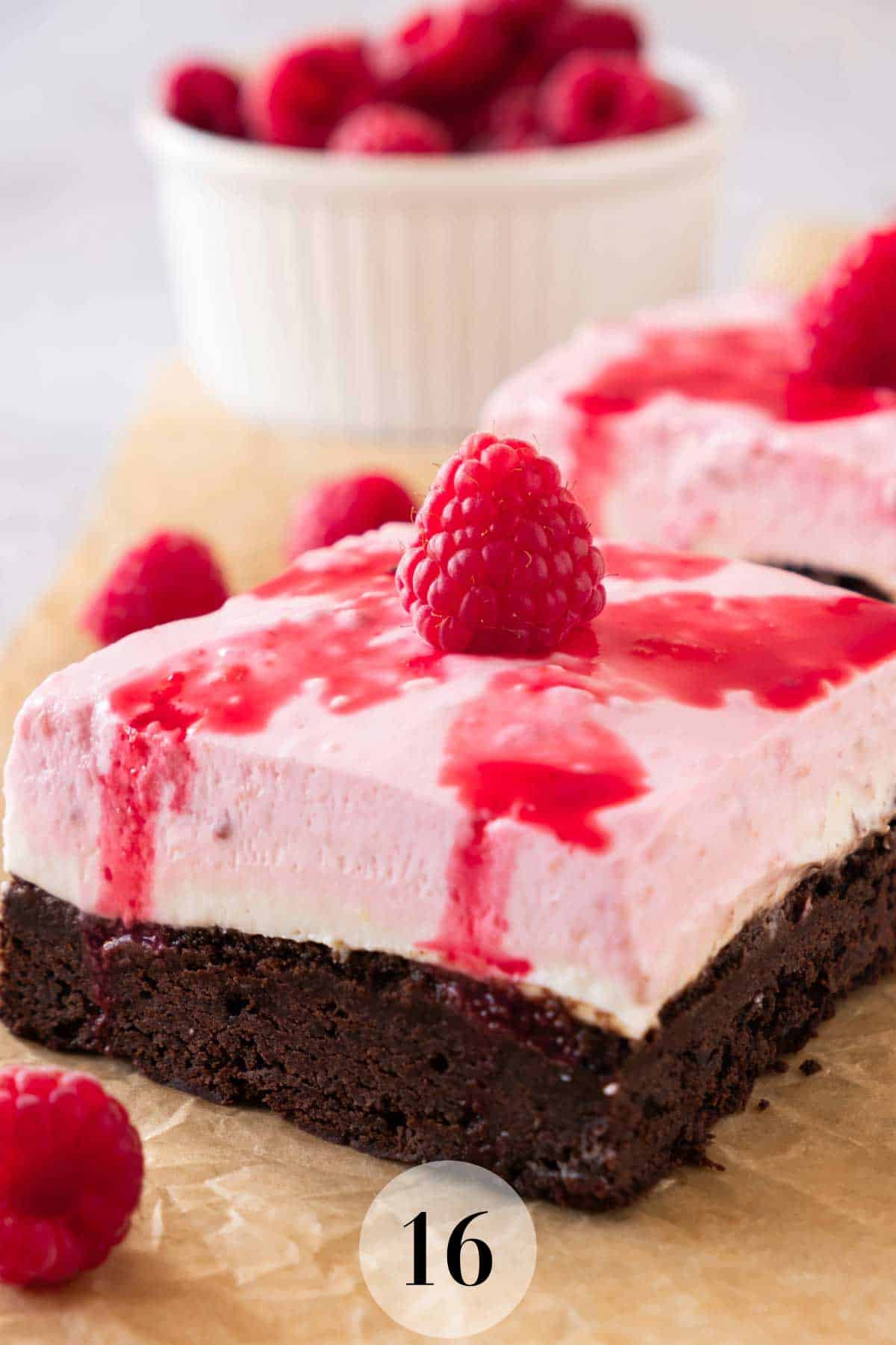 A square of raspberry cheesecake brownie drizzled with raspberry juice and a raspberry on top. 