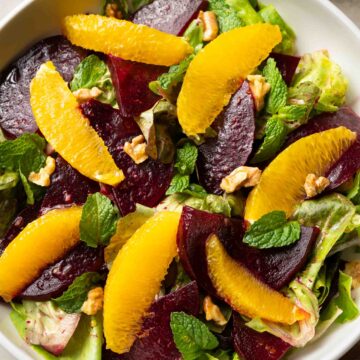 A colorful beet and orange salad with walnuts and mint leaves, accompanied by a vinaigrette dressing on the side.
