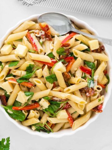 A bowl of penne pasta with spinach, sun-dried tomatoes, and herbs.