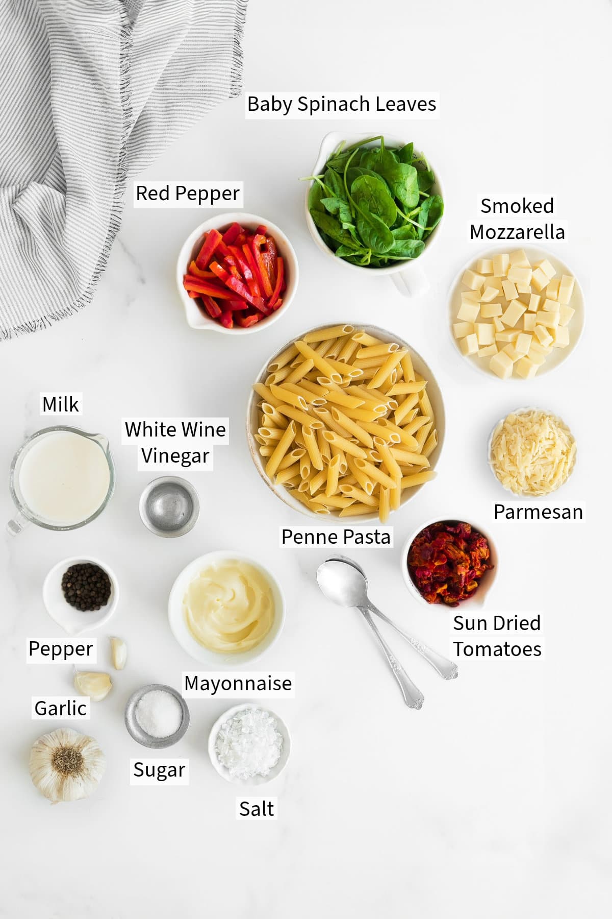 Ingredients for a smoked mozzarella pasta salad recipe arranged on a white surface, each labeled with its name.