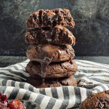 A stack of chocolate cookies with melted chocolate drizzling down on a striped cloth.