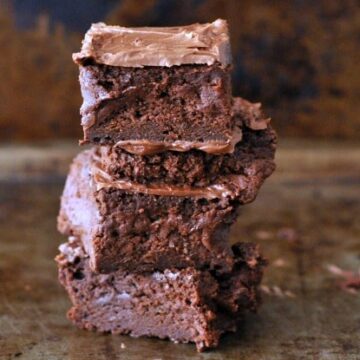 Three chocolate brownies with frosting, stacked on a baking sheet.