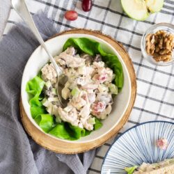 A bowl of Waldorf chicken salad with grapes and walnuts served on lettuce leaves, presented on a striped tablecloth.
