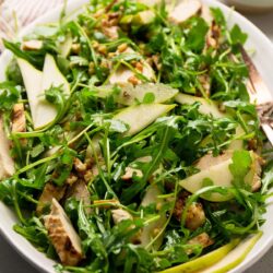 A plate of arugula salad with sliced pears and chicken.
