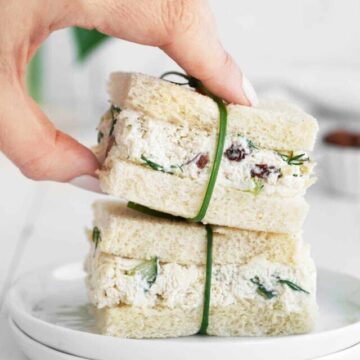A hand holding a stack of chicken salad sandwiches tied with a chive strand.