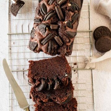 Chocolate loaf cake with cookies on top, partially sliced.
