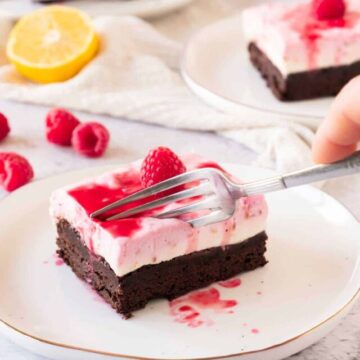 A person using a fork to take a piece from a square of Raspberry Cheesecake brownie.