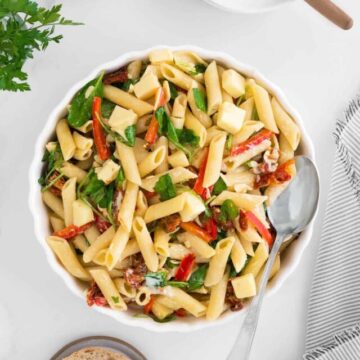 Penne pasta with spinach, sun-dried tomatoes, and cheese, served with slices of bread on a white table.