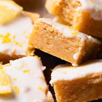 Slices of lemon brownies with zest topping on a wooden surface.