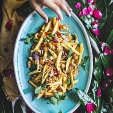 A hand reaching out to a plate of Thai green mango salad.