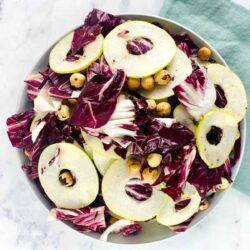 A bowl of salad with sliced pears, radicchio, and hazelnuts.