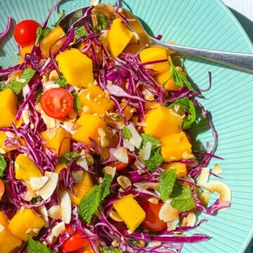 A colorful salad with mango, red cabbage, cherry tomatoes, and herbs served on a light blue plate.