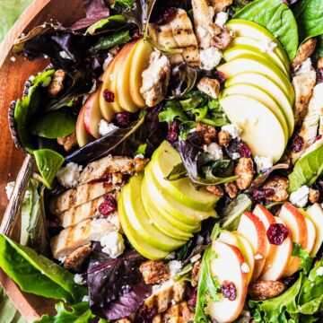 A colorful apple walnut salad with grilled chicken arranged in a wooden bowl.