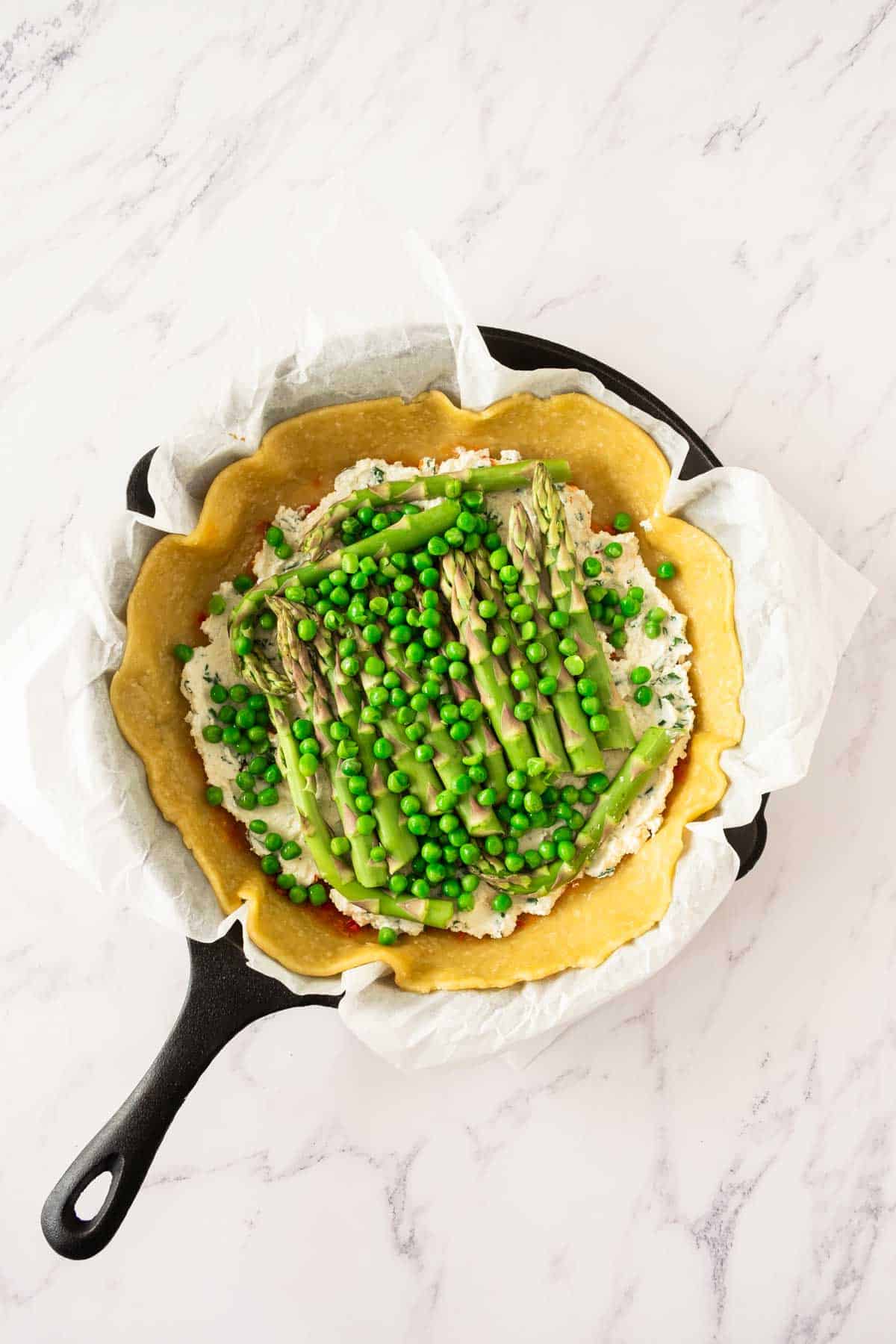 A gelette pastry base in a cast iron pan with asparagus and peas.