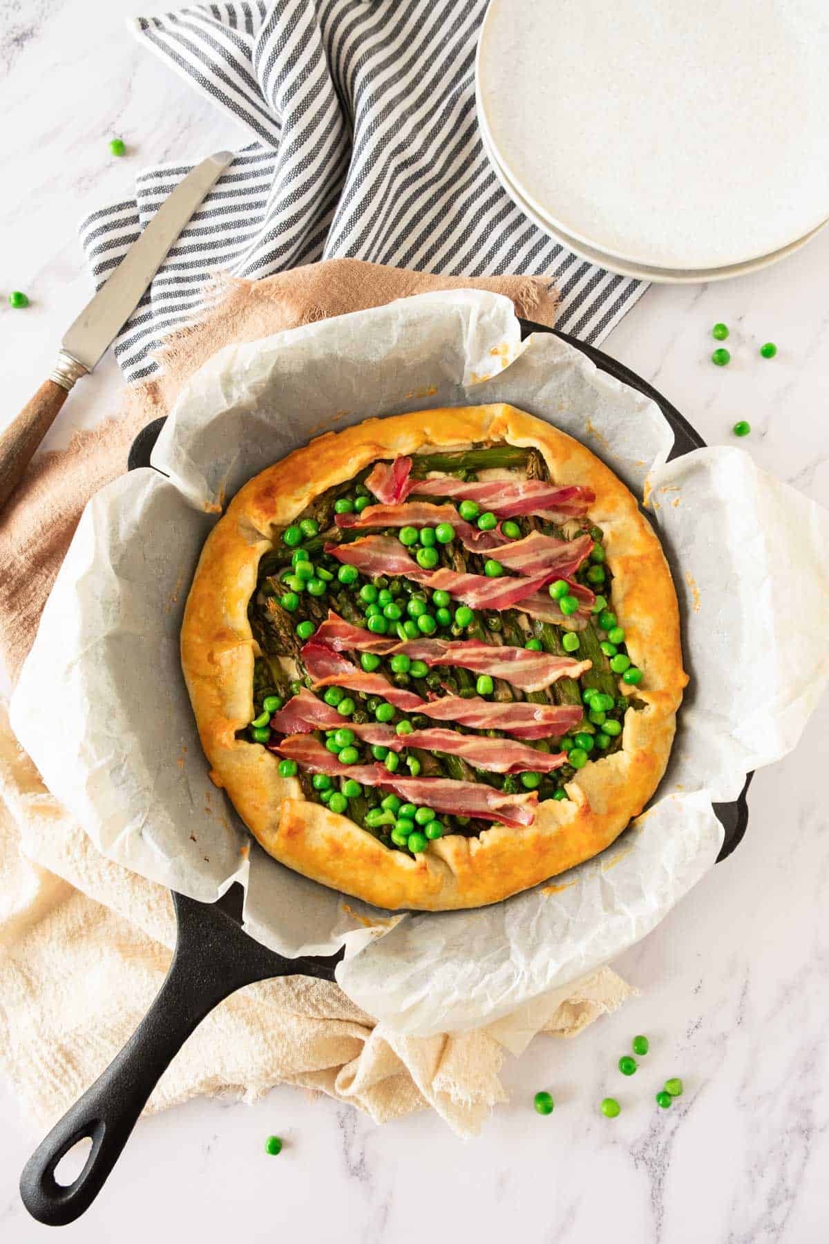 A cooked asparagus galette in a cast iron pan with bacon and peas.