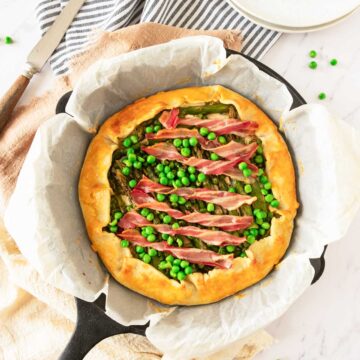 A cooked asparagus galette in a cast iron pan with bacon and peas.