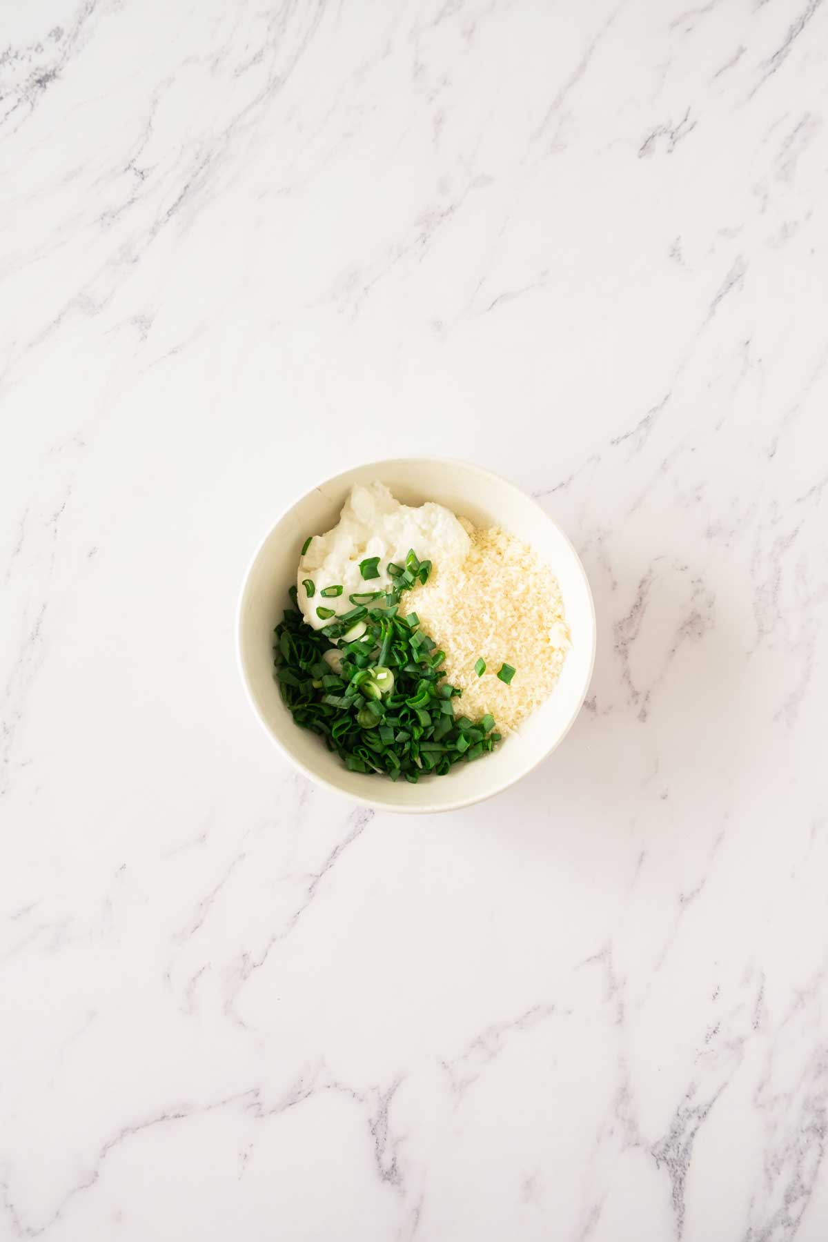 A bowl with cottage cheese, parmesan and herbs on a marble table.