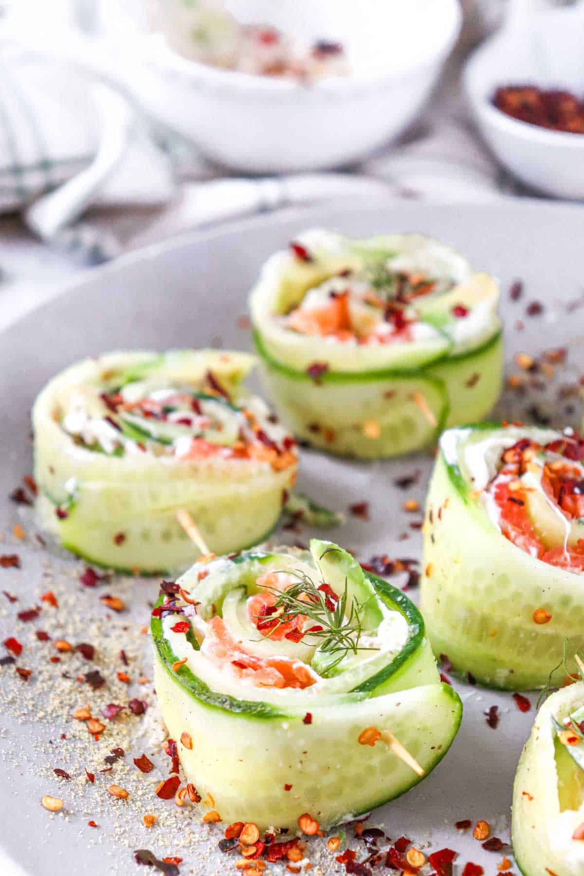 Cucumber rolls filled with cream cheese, smoked salmon, and dill, sprinkled with spices on a white plate.