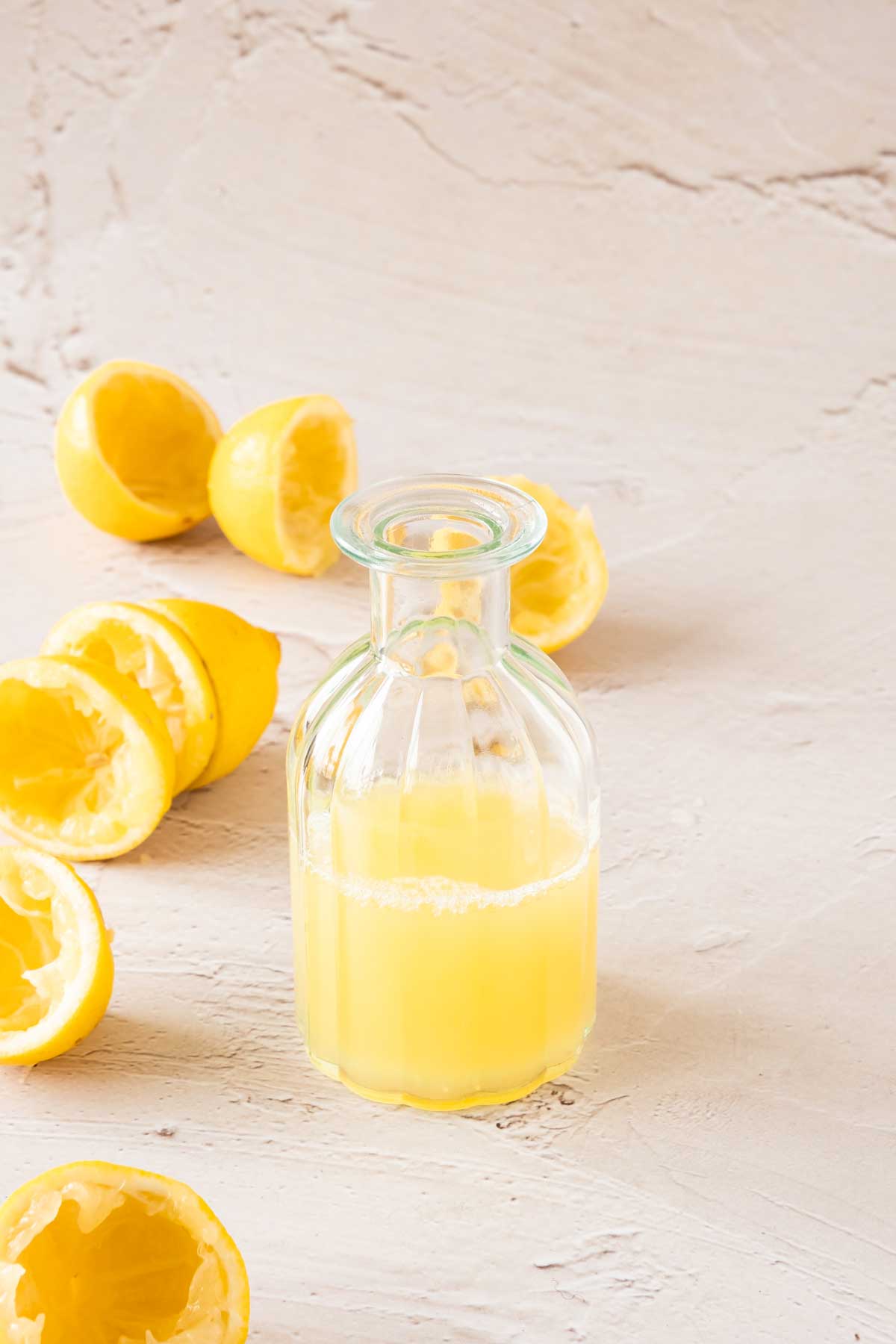 A bottle of lemon juice surrounded by squeezed lemons.
