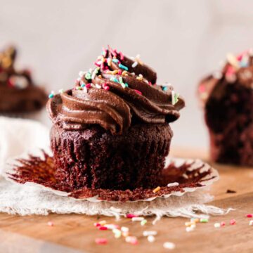 A chocolate cupcake with creamy frosting topped with colorful sprinkles on a wooden surface.