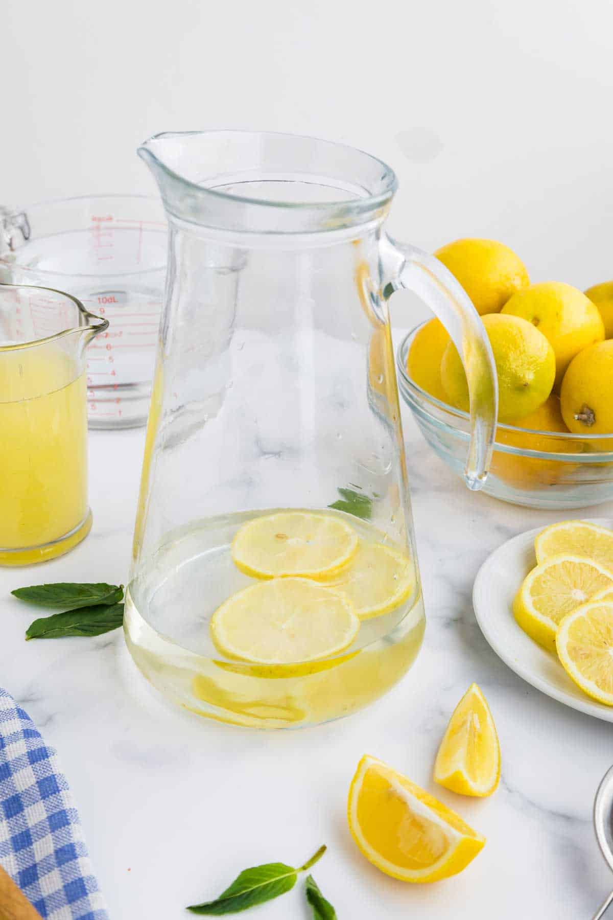 A pitcher of water with lemon slices, surrounded by ingredients and kitchenware.
