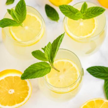 Four glasses of lemonade garnished with mint leaves and lemon slices.